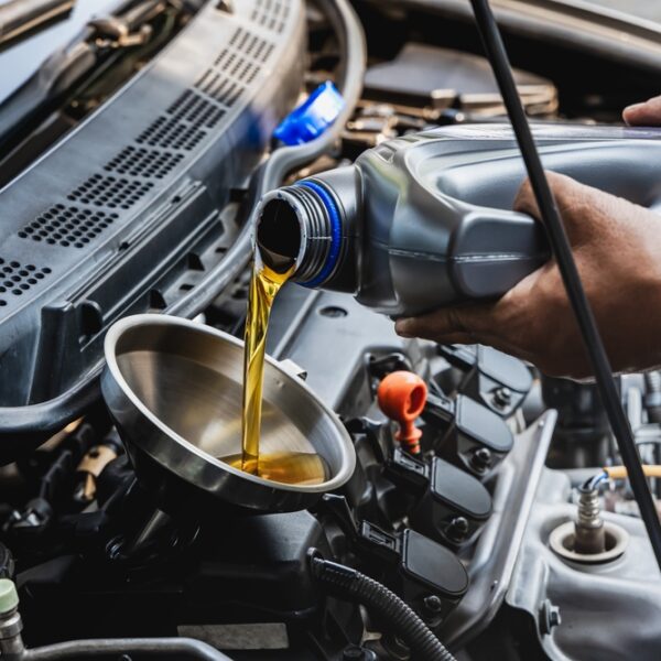 Car mechanic pouring engine oil into vehicle during doing car maintenance in garage